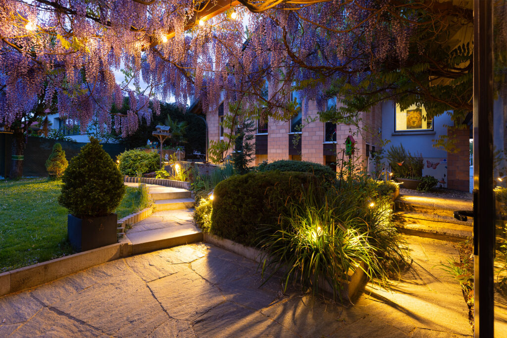 Exterior view at dusk, with warm lighting illuminating the garden path and steps leading to the studio entrance.